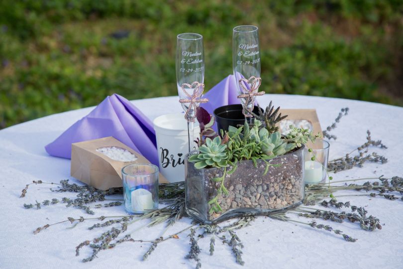 A round table decorated with dried lavender flowers, a succulent arrangement, tealights, glass champagne flutes, and lavender napkins.